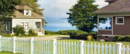Two houses on the coast with water in the background.